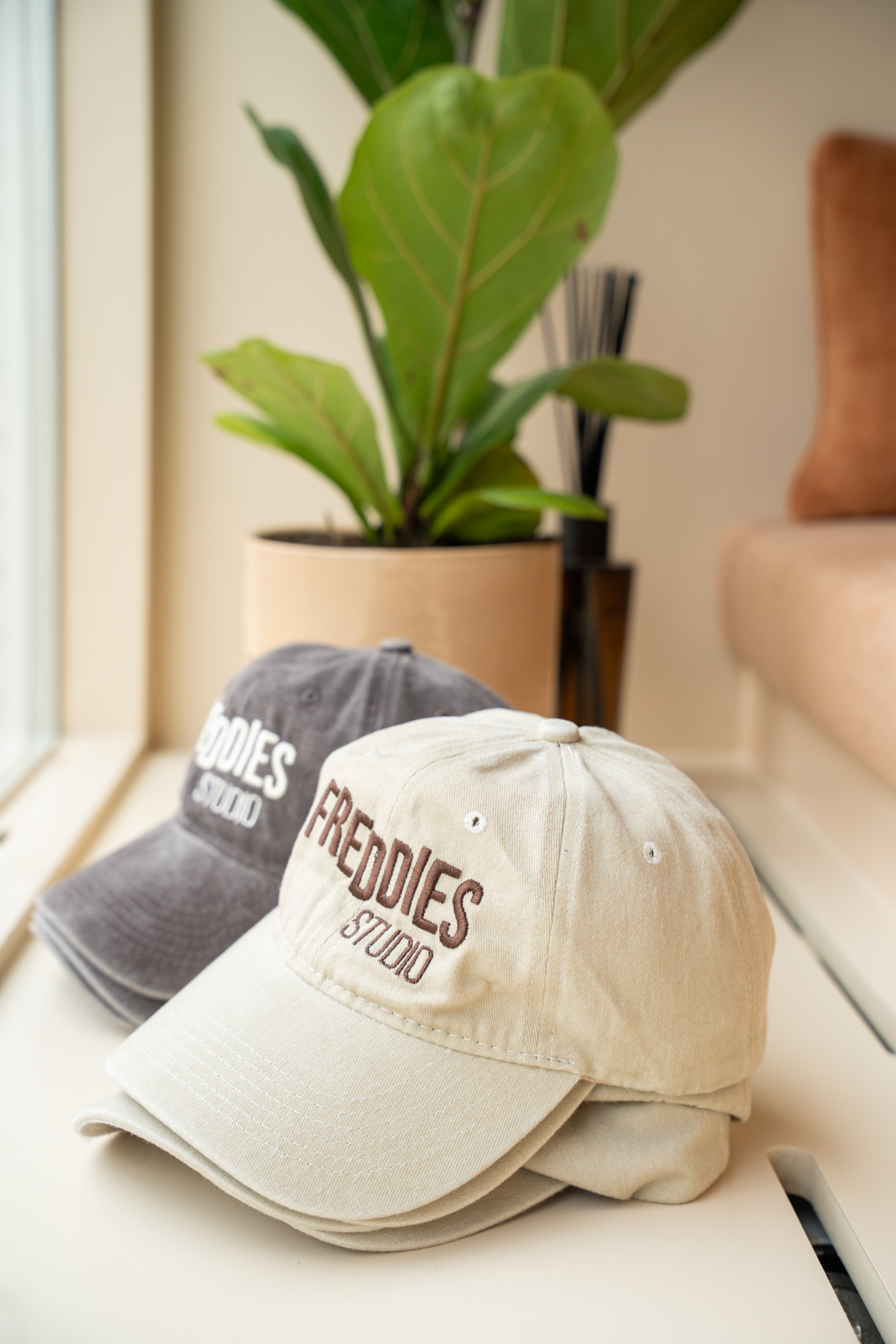 freddies-studio-bussum-close-up-beige-freddies-studio-pet-met-logo-naast-grijze-pet-en-plant