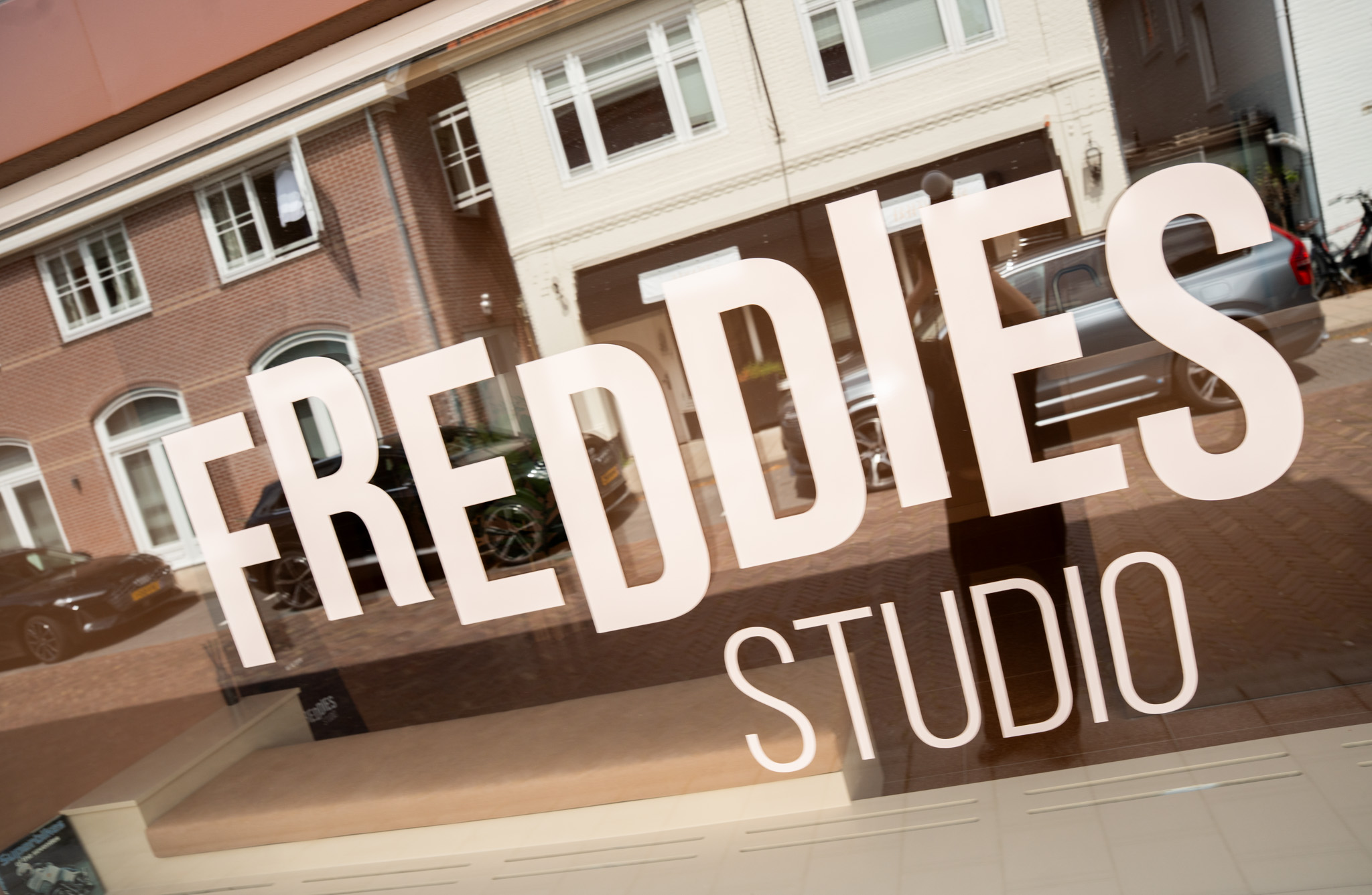 freddies studio bussum close up etalageraam met logo en spiegeling straatbeeld