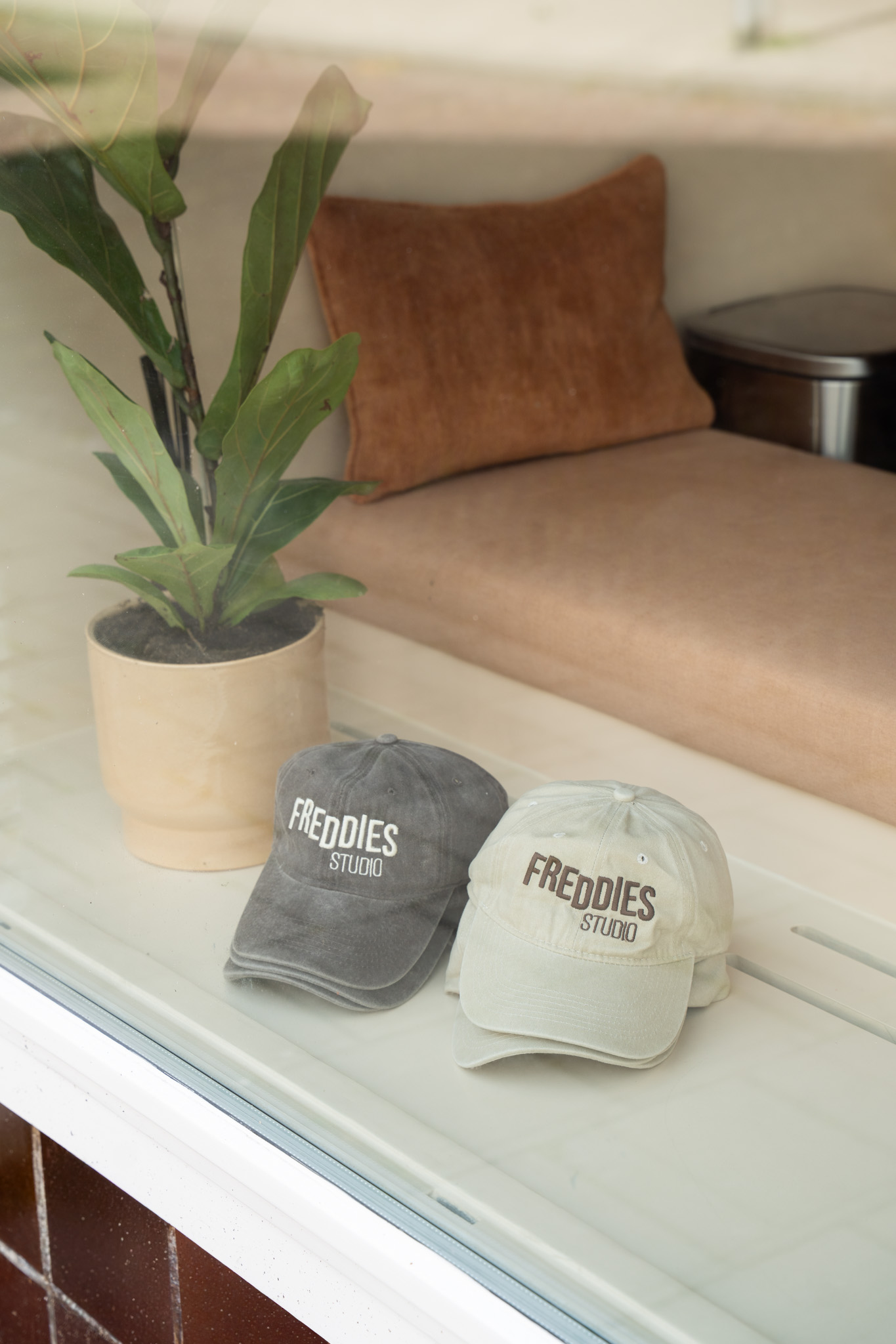 freddies-studio-bussum-close-up-twee-freddies-studio-petten-op-vensterbank-naast-plant-en-kussen