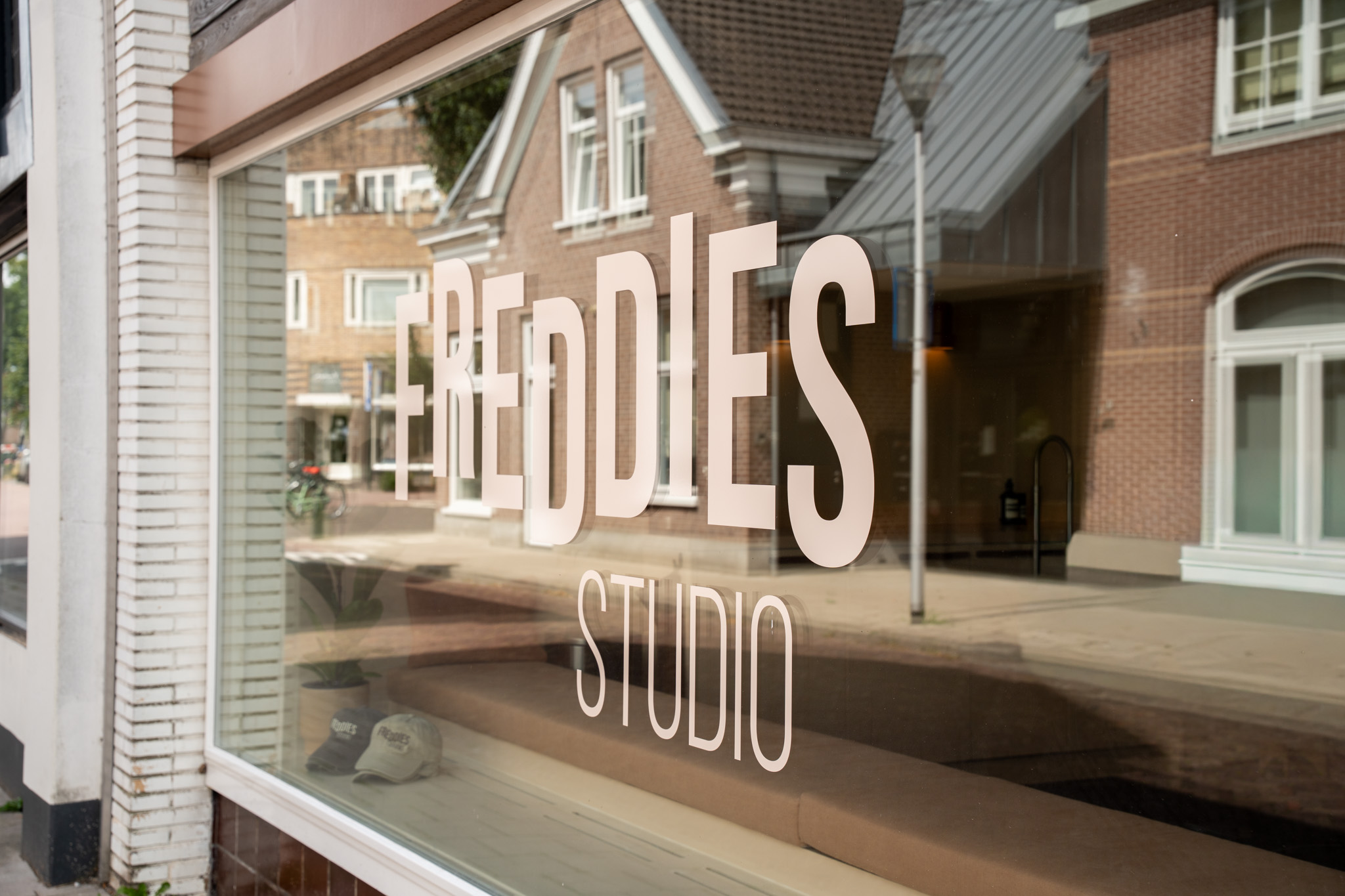 freddies studio bussum etalageraam met logo en spiegeling straatbeeld petten op vensterbank