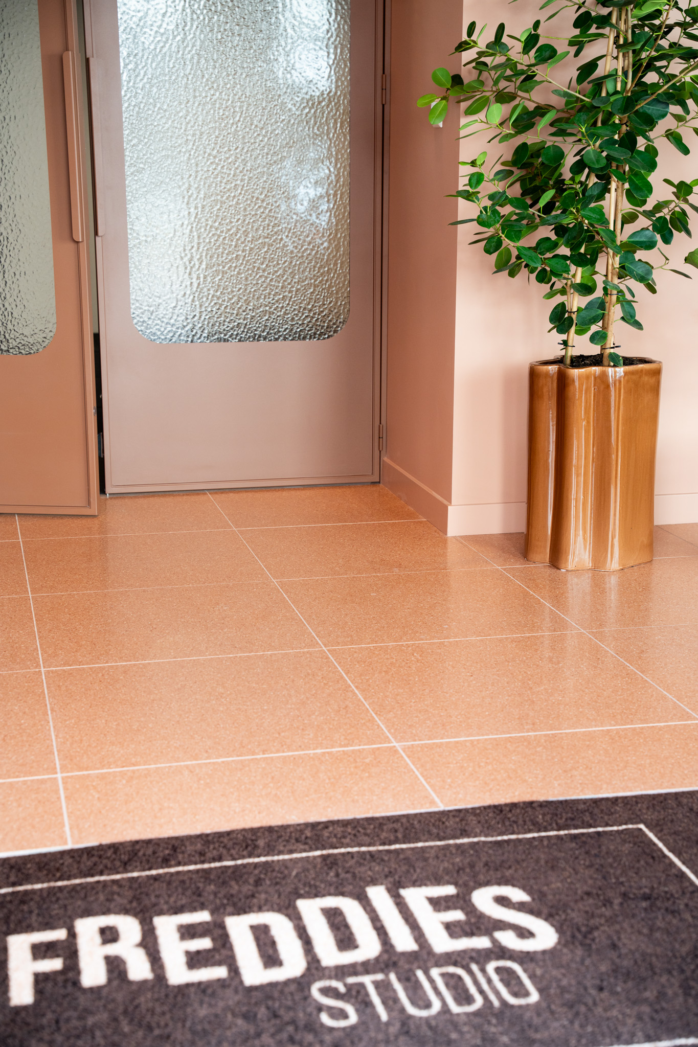 freddies-studio-bussum-hoek-met-plant-in-koperen-pot-en-deurmat-op-vloer