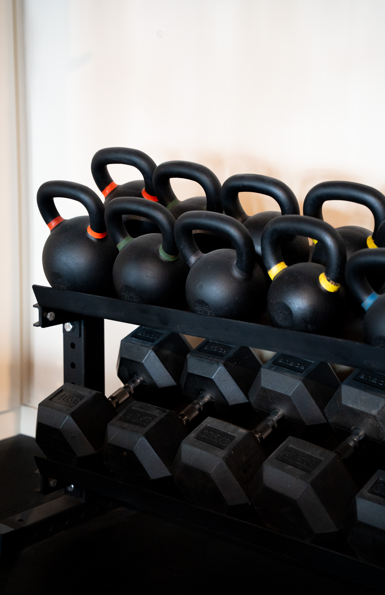 freddies-studio-bussum-kettlebells-met-gekleurde-handvatten-op-rek-boven-hexagonale-dumbbells
