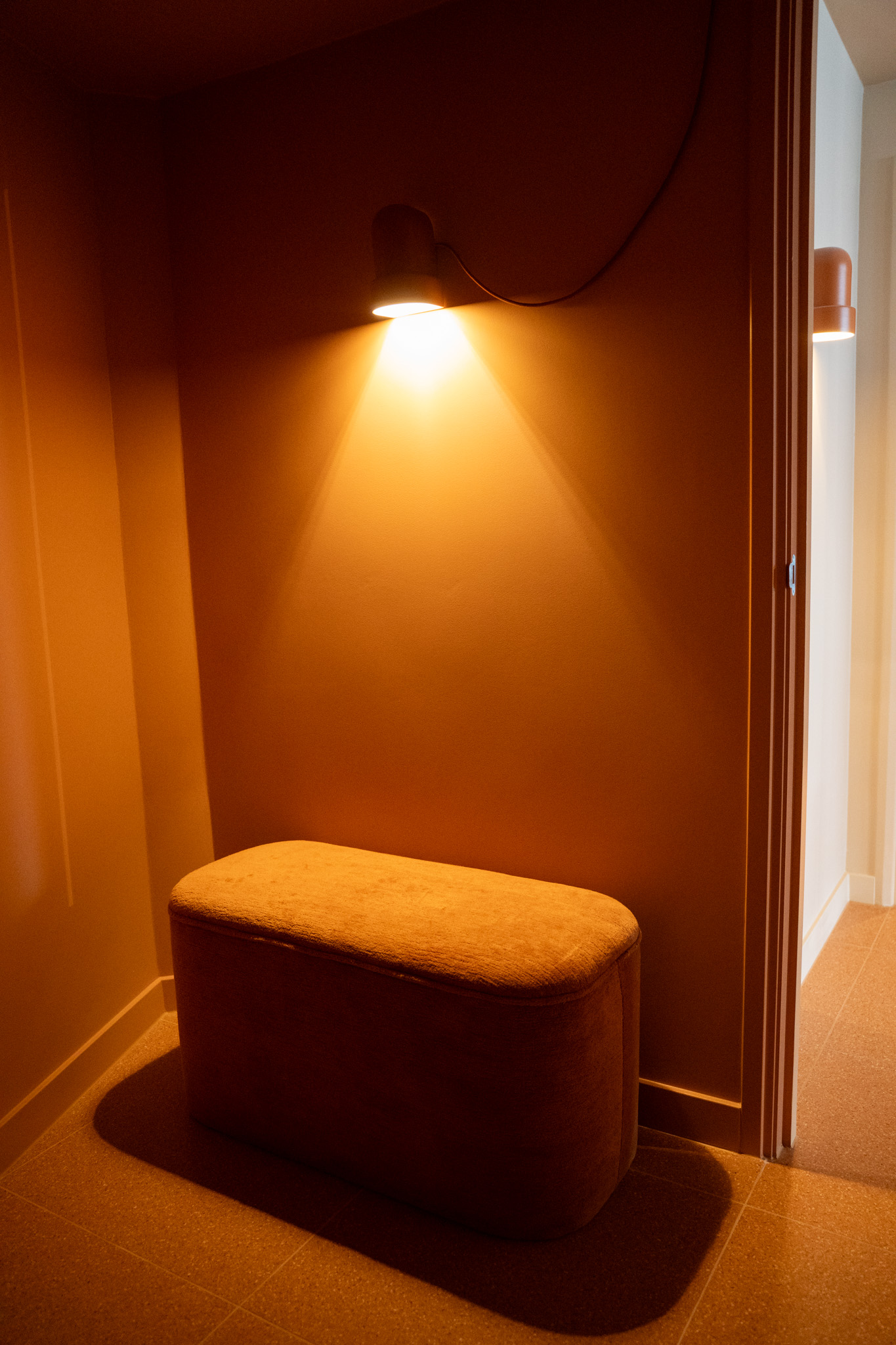 freddies-studio-bussum-kleedruimte-hoek-met-terracotta-bankje-wandlamp-en-deur-naar-douche