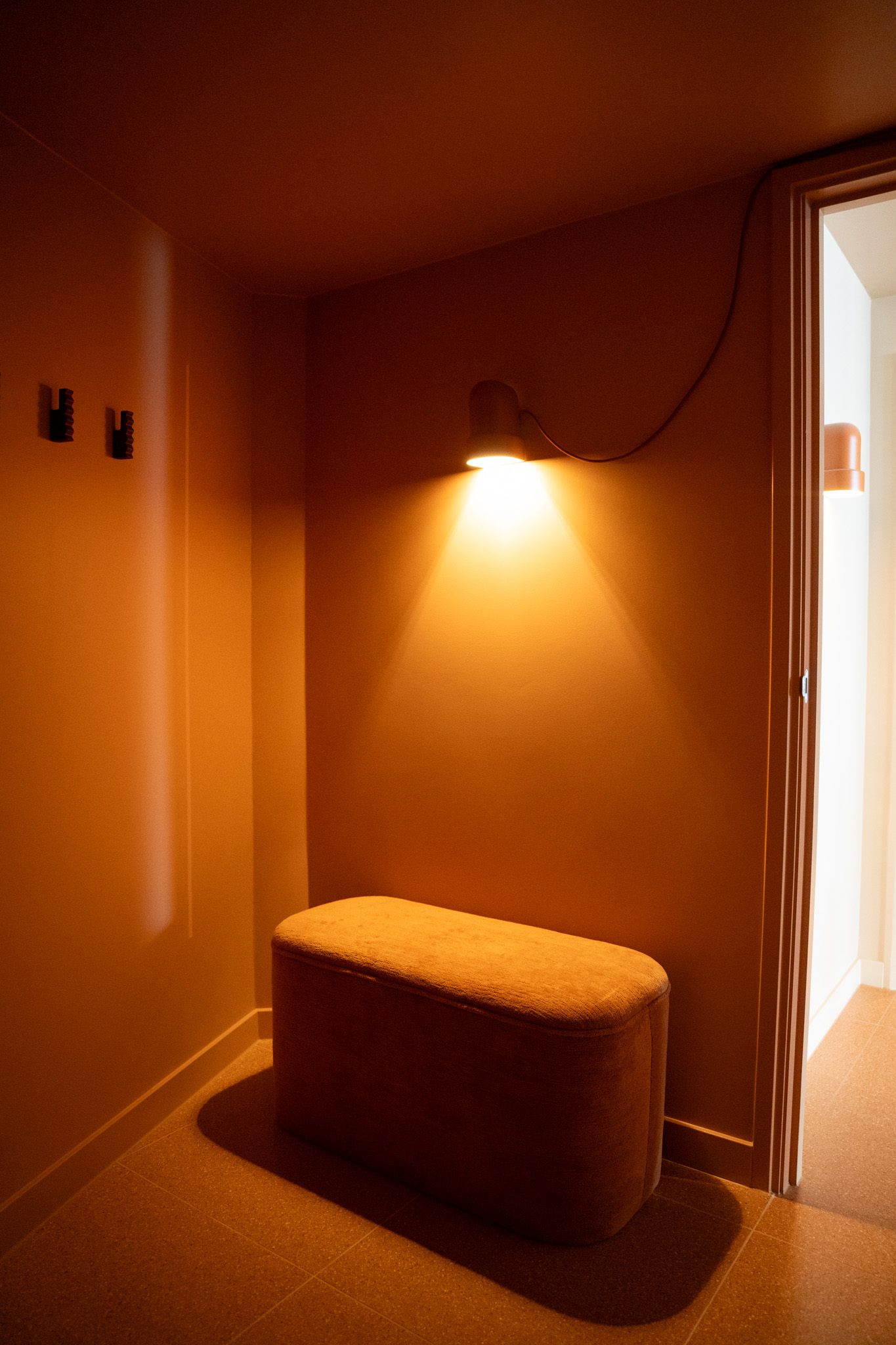 freddies-studio-bussum-kleedruimte-hoek-terracotta-bankje-wandlamp-met-deur-en-kledinghaakjes