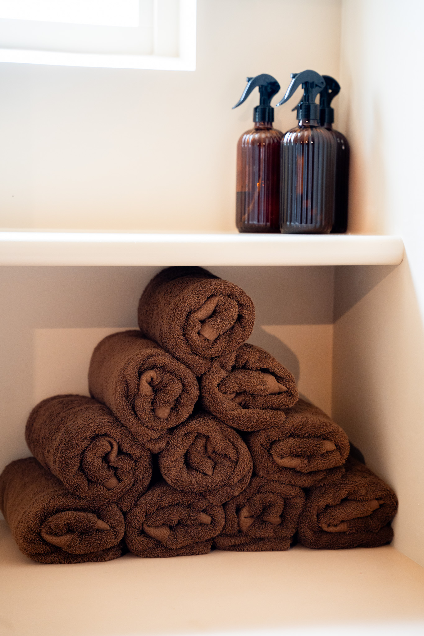 freddies-studio-bussum-opgerolde-bruine-handdoeken-op-plank-met-sprayflacons