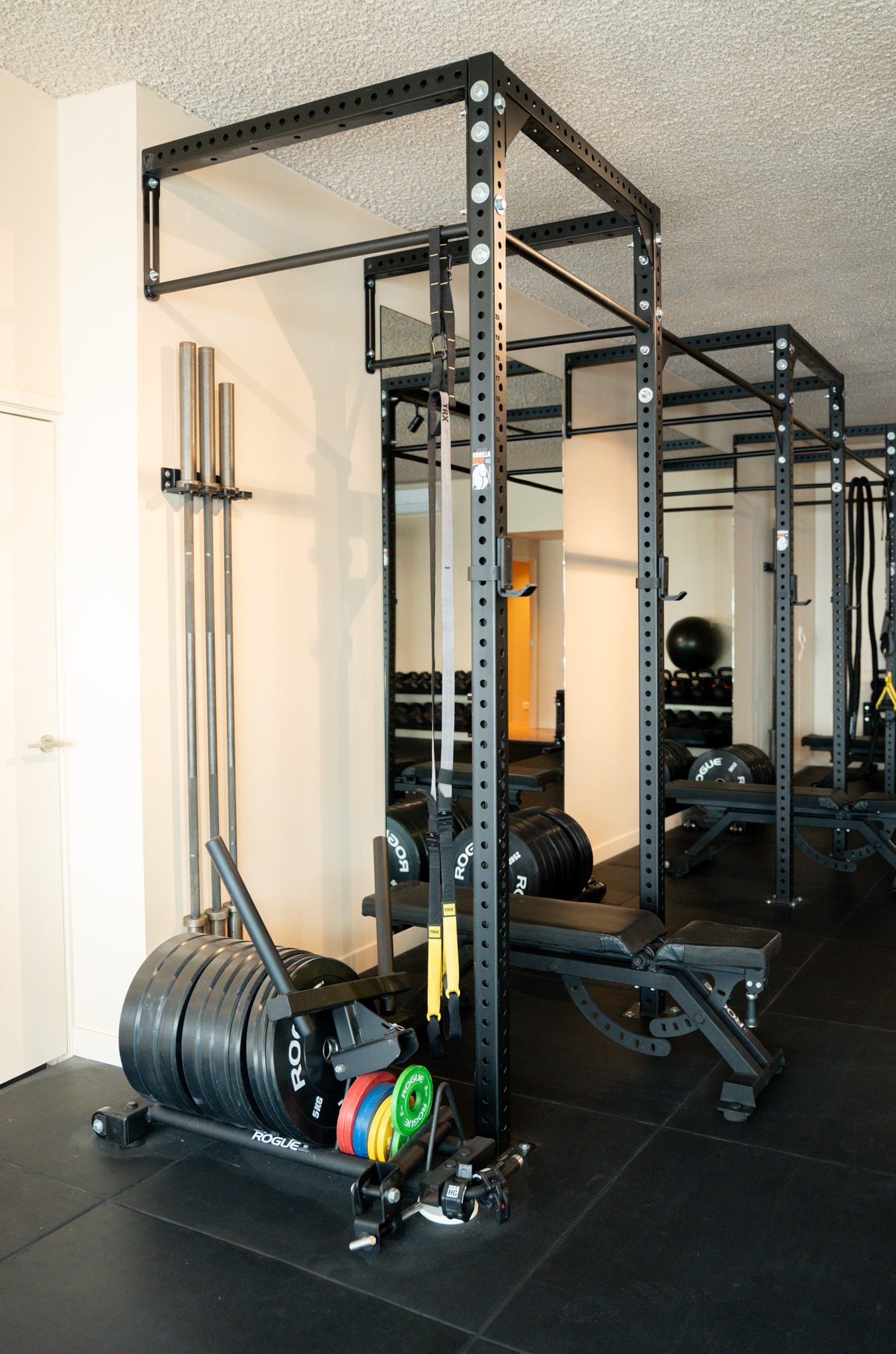freddies-studio-bussum-power-rack-met-opgehangen-barbells-rogue-gewichtsschijven-en-trx-banden